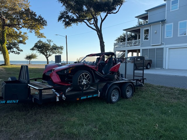 Red Polaris Slingshot on black car hauler trailer near beachfront